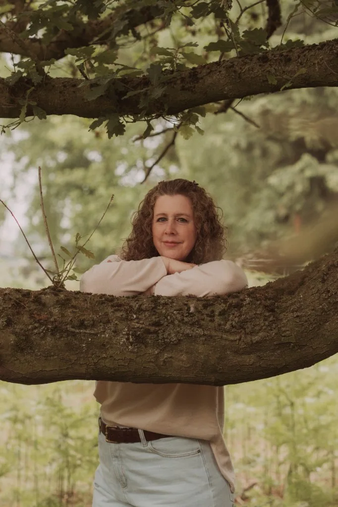 Ally outdoors, leaning gently on a tree branch in soft natural light