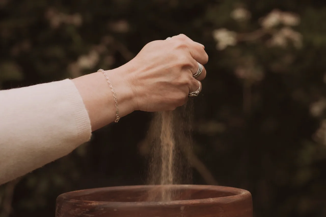 A hand letting sand pour slowly into a bowl outdoors — a calming, grounding image symbolising release and the decision to slow down.