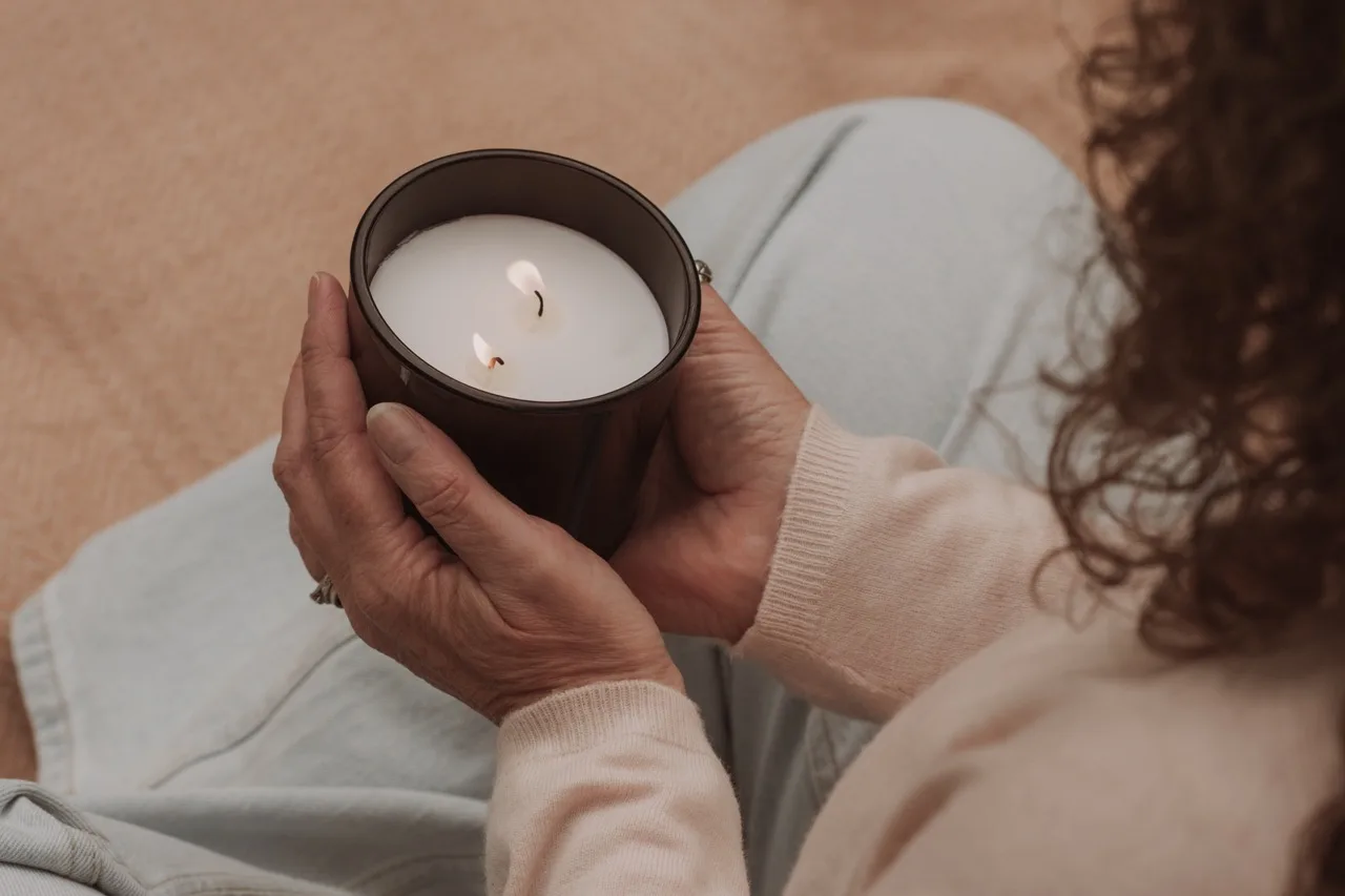 Hands cradling a softly lit candle in warm natural light — a quiet moment of self-care that suggests therapy as care, not only crisis response.