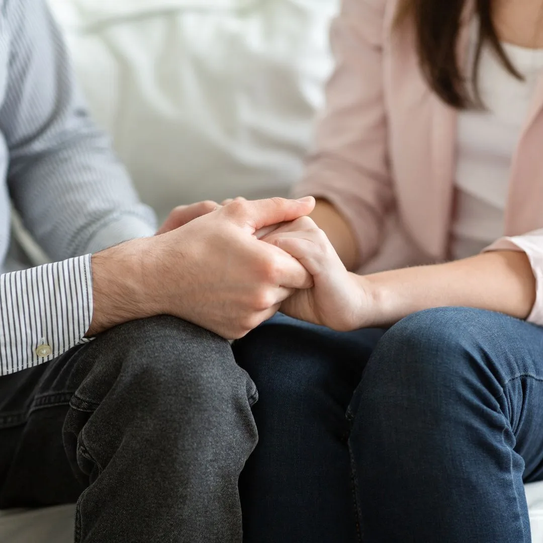 A couple sitting on a sofa with hands gently held together — a small, intimate image of communication, support and connection.