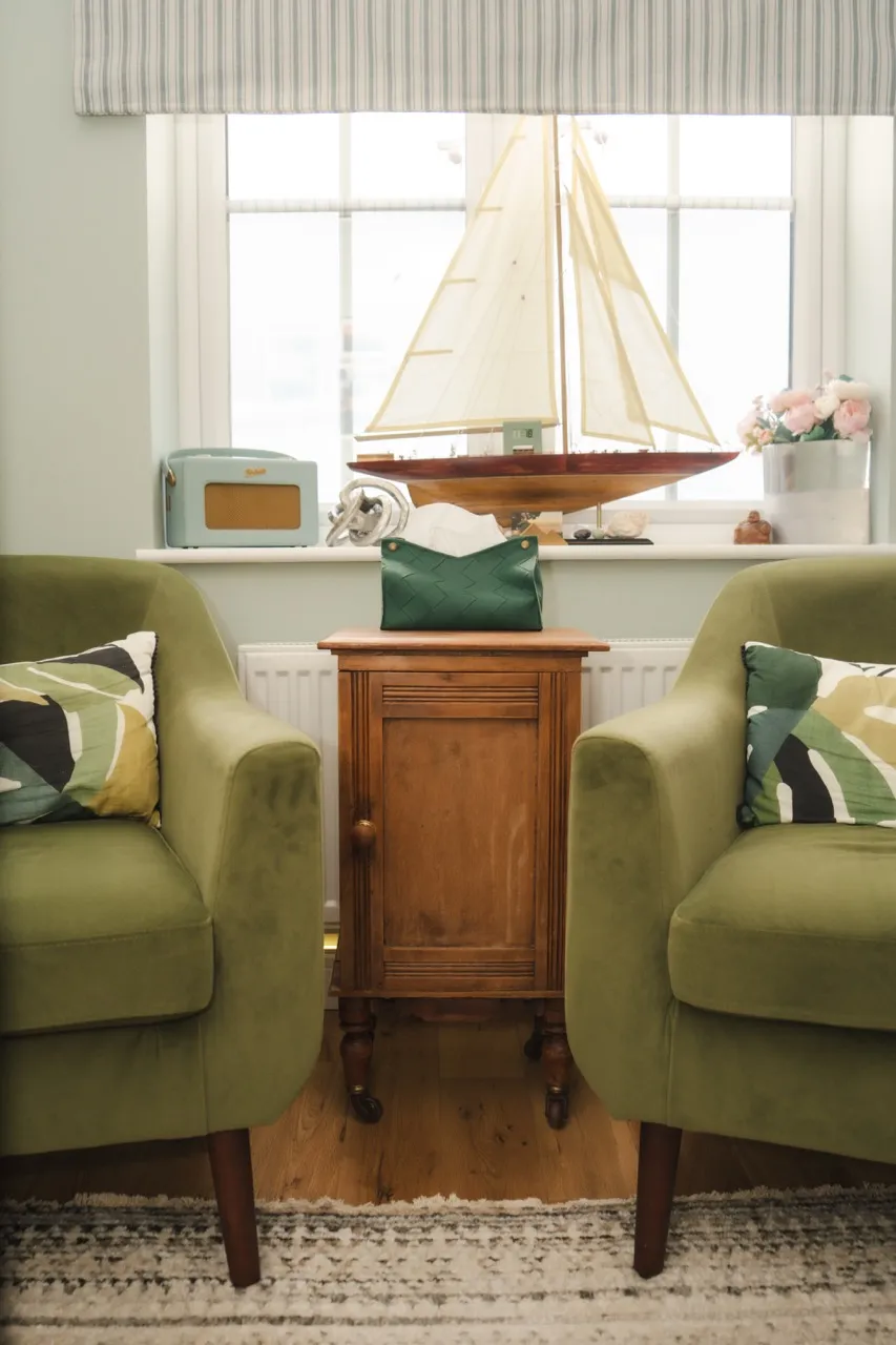 Ally's calm therapy room — two sage-green velvet armchairs facing each other beside a sunlit window, ready for a session.